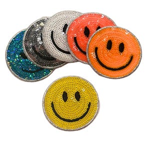 Puede incluir: Parches de lentejuelas con caras sonrientes en varios colores: azul, plateado, naranja y amarillo. Cada parche tiene una cara sonriente negra y un borde plateado. Parches redondos para ropa o accesorios.