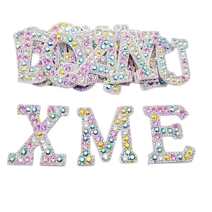 May include: A set of colorful rhinestone letters spelling out "DON'T X ME". The letters are made of white metal and are covered in iridescent rhinestones.