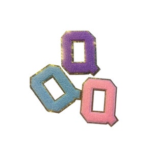 Puede incluir: Tres parches de letras de fieltro en forma de la letra Q. Los parches son morado, azul y rosa con ribete dorado.
