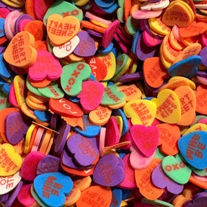 Pode incluir: Um grande monte de doces coloridos em forma de coração com várias mensagens, incluindo "Love", "Sweet Kisses", "Be Mine" e "XOXO".