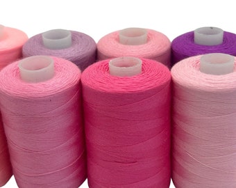 May include: A set of seven spools of thread in various shades of pink and purple. The spools are arranged in a row, with the darkest shade of purple on the right and the lightest shade of pink on the left.