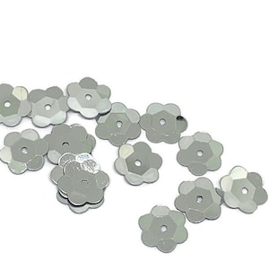 Puede incluir: Paillettes plateadas en forma de flor con un agujero en el centro.