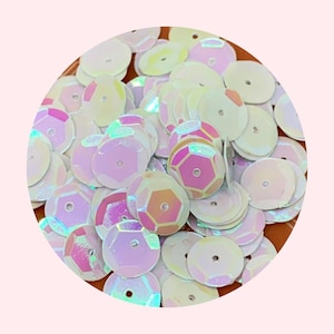 May include: A pile of iridescent white sequins with a holographic finish. The sequins are round and have a small hole in the center.