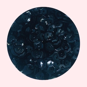 May include: A close-up of a pile of dark blue sequins. The sequins are small and round, with a slightly iridescent finish.