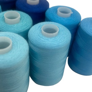 May include: A selection of blue thread spools, ranging from pale turquoise to dark navy. Each spool features a white plastic core. The tightly wound threads indicate a high-quality sewing material, ideal for a variety of craft projects.