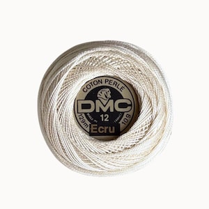 Puede incluir: Un ovillo de hilo de bordar DMC Coton Perlé, tamaño 12, con un peso de 10g y una longitud de 129m. La etiqueta central muestra el logotipo de DMC, el texto Coton Perlé, Made in France y el nombre del color Ecru en letras negras.