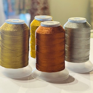 Può includere: Quattro bobine di filo metallico in colori oro, rame e argento. Le bobine sono su basi di plastica bianca.