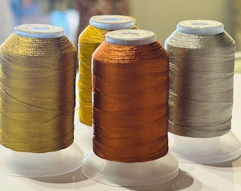 May include: Four spools of metallic thread in gold, copper, and silver colors. The spools are on white plastic bases.