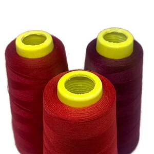 May include: Three spools of thread, one red, one burgundy, and one dark red. The spools have yellow plastic tops.