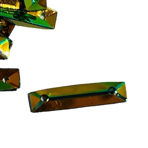 May include: A close-up of iridescent green and gold rectangular and triangular shaped rhinestones.