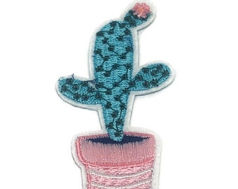 May include: A blue cactus with a pink flower on top, potted in a pink pot with white stripes. The cactus is embroidered on a white background.