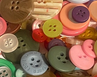 May include: A collection of colorful buttons in various shapes, sizes, and materials. Some buttons have a striped pattern, while others have a solid color. There are also buttons with different numbers of holes. The buttons are a mix of plastic, metal, and fabric.