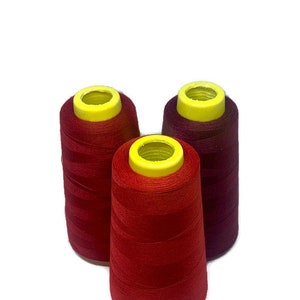 May include: Three spools of thread, one red, one burgundy, and one dark red. The spools are all the same size and have yellow plastic tops.