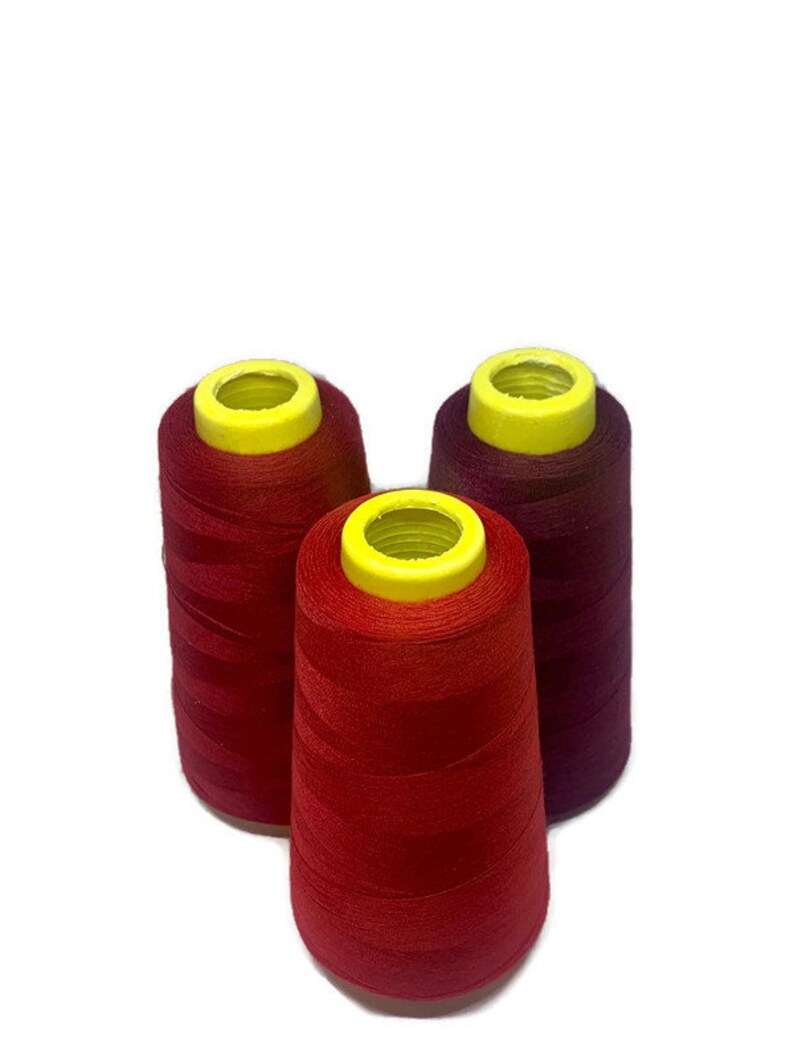 May include: Three spools of thread, one red, one burgundy, and one dark red. The spools are all the same size and have yellow plastic tops.