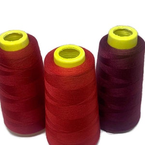 May include: Three spools of thread, one red, one burgundy, and one orange. The spools are all the same size and have yellow plastic tops.