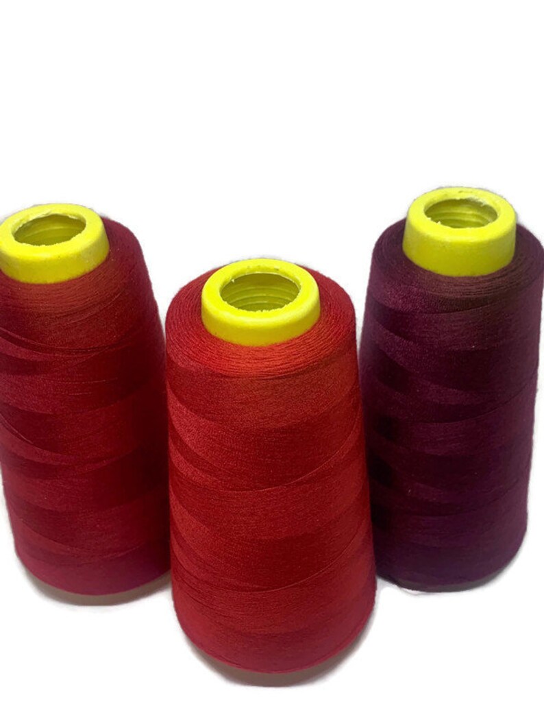 May include: Three spools of thread, one red, one burgundy, and one orange. The spools are all the same size and have yellow plastic tops.