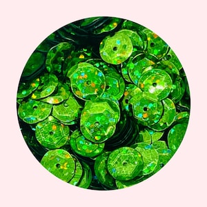 May include: A close-up of a pile of green iridescent sequins. The sequins are round and have a holographic finish.