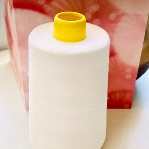 May include: A white spool of thread with a yellow plastic top. The spool is sitting on a white surface.