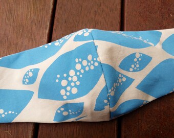 May include: A blue and white fabric face mask with a pattern of white leaves on a blue background. The leaves have a pattern of white dots.