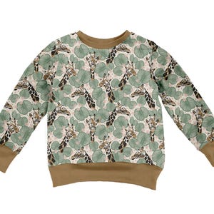 May include: A long-sleeve sweatshirt featuring a repeating pattern of giraffe heads and green tropical leaves on a light background. The garment has a solid brown crew neckline, sleeve cuffs, and a bottom hem, providing a contrast to the print.