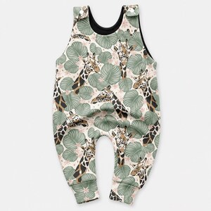 May include: A sleeveless romper featuring a repeating pattern of giraffes and large green tropical leaves on a light background. The garment has a black inner lining and two white snap buttons at the top of the shoulder straps for closure.