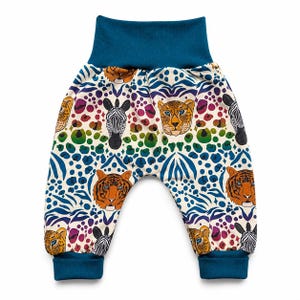 May include: Pants with a high teal waistband and matching teal cuffs at the ankles. The fabric features a cream background with a repeating pattern of animal faces including tigers, zebras, and leopards, interspersed with rainbow-colored spots.