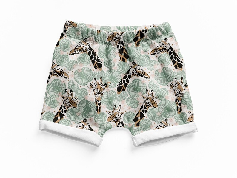 May include: Shorts featuring an all-over print of giraffe heads and light green tropical leaves on a pale background. The garment has an elasticized waistband and white cuffed leg openings, providing a structured look with a repeating pattern.