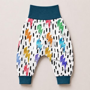 May include: Pull-on pants featuring a white background with a pattern of multicolored watercolor lightning bolts and black vertical dashes. The garment includes a wide, solid dark teal elastic waistband and matching dark teal ankle cuffs.