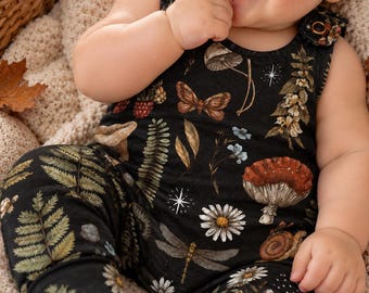 May include: A black sleeveless romper featuring a detailed print of ferns, mushrooms, butterflies, dragonflies, snails, and daisies. The garment has round metallic snap closures at the shoulders and cuffed pant legs, showcasing a nature-inspired pattern.
