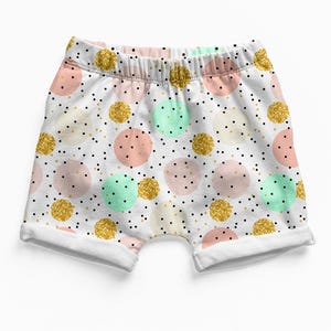 K&ouml;nnte beinhalten: Wei&szlig;e Shorts mit elastischem Bund und einem Muster aus Punkten in Pastellrosa, Mintgr&uuml;n und glitzerndem Gold. Der Stoff ist mit kleinen schwarzen Punkten &uuml;bers&auml;t, die &uuml;ber die gesamte Oberfl&auml;che verteilt sind, mit umgeschlagenen S&auml;umen.