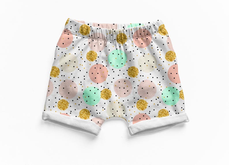 K&ouml;nnte beinhalten: Wei&szlig;e Shorts mit elastischem Bund und einem Muster aus Punkten in Pastellrosa, Mintgr&uuml;n und glitzerndem Gold. Der Stoff ist mit kleinen schwarzen Punkten &uuml;bers&auml;t, die &uuml;ber die gesamte Oberfl&auml;che verteilt sind, mit umgeschlagenen S&auml;umen.