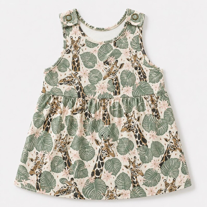 May include: A sleeveless dress featuring a repeating pattern of giraffes, green tropical leaves, and small pink flowers on a cream background. The garment has a gathered waistline and two metallic snap buttons on the shoulder straps for closure.