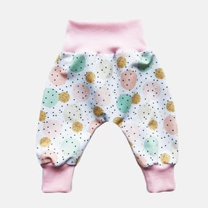 K&ouml;nnte beinhalten: Hose mit wei&szlig;em Hintergrund und einem Muster aus mintgr&uuml;nen, zartrosa und goldglitzernden Kreisen, akzentuiert durch kleine schwarze Punkte. Das Kleidungsst&uuml;ck hat einen breiten, einfarbigen hellrosa Elastikbund und passende hellrosa Beinb&uuml;ndchen.