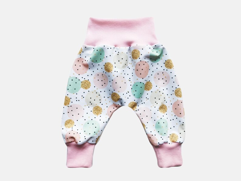 K&ouml;nnte beinhalten: Hose mit wei&szlig;em Hintergrund und einem Muster aus mintgr&uuml;nen, zartrosa und goldglitzernden Kreisen, akzentuiert durch kleine schwarze Punkte. Das Kleidungsst&uuml;ck hat einen breiten, einfarbigen hellrosa Elastikbund und passende hellrosa Beinb&uuml;ndchen.