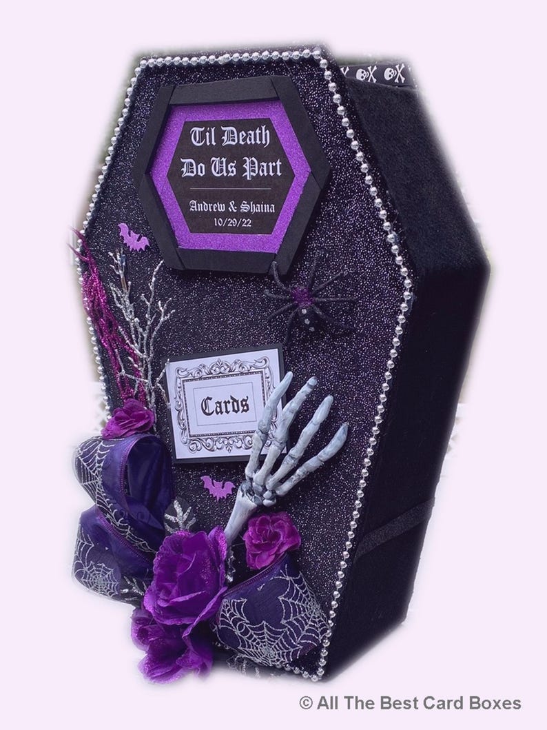 Puede incluir: Una caja de tarjetas negra en forma de ata&uacute;d con un acabado de purpurina morada. La caja est&aacute; decorada con una telara&ntilde;a blanca, una mano de esqueleto y un lazo morado. La caja tiene un letrero que dice "Til Death Do Us Part" con los nombres "Andrew & Shaina" y la fecha "10/20/22".