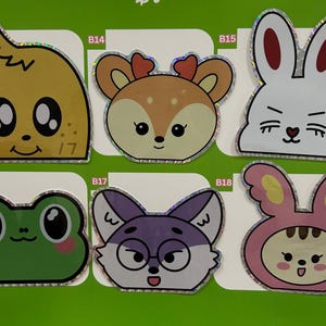May include: A collection of colorful, cartoon animal stickers. The stickers include a yellow creature, a deer, a white bunny, a green frog, a purple fox, and a pink bunny. Each sticker has a holographic border.
