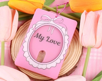 May include: Pink plastic card holder with a white lace design and the words "My Love" in a white oval. The card holder has a hole for a chain or string.