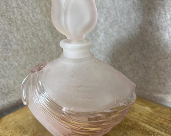 May include: A pale pink frosted glass perfume bottle featuring a sculptural tulip-shaped stopper. The body of the bottle has a rounded, asymmetrical shape with swirling, clear glass ridges that wrap around the lower section, contrasting with the matte, satin-like finish of the upper portion.