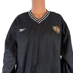 May include: Black Reebok pullover jacket with a V-neck collar. The collar has white and black stripes. The Reebok logo is on the left chest. The right chest has a "Wicked" logo in red, yellow, and brown.