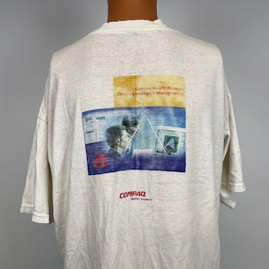 Peut inclure: T-shirt blanc avec un logo Compaq vintage et un graphique de deux personnes travaillant sur des ordinateurs. Le texte sur le graphique indique "Compaq Insight Manager Compaq Intelligent Manageability".