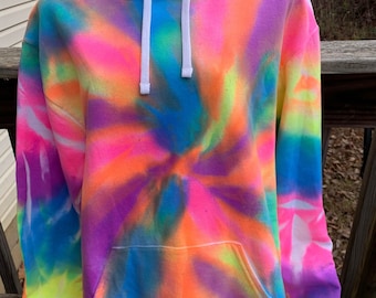 May include: A vibrant tie-dye hoodie in a swirl pattern, featuring a spectrum of colors including neon pink, orange, yellow, blue, and purple. The hoodie has a kangaroo pocket, a drawstring hood, and ribbed cuffs. The garment is displayed on a black mannequin.