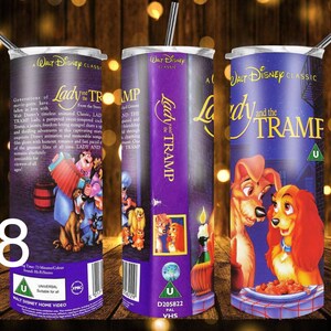 Puede incluir: Un vaso de acero inoxidable morado y blanco con un dise&ntilde;o de la cinta VHS de La Dama y el Vagabundo. El dise&ntilde;o incluye el t&iacute;tulo de la pel&iacute;cula, un logotipo de Universal y una imagen de Lady y Tramp compartiendo un plato de espaguetis.