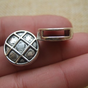 May include: Two silver metal bead caps, one with a square grid pattern and the other with a rectangular opening.