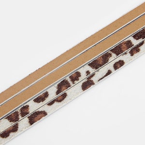 May include: Close-up of a brown and white leopard print ribbon with a tan suede backing.