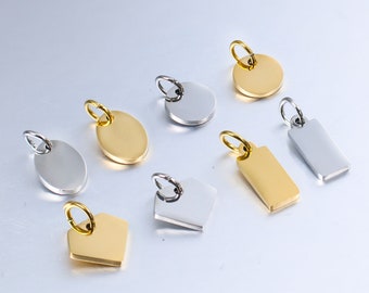 May include: A set of eight blank metal charms in silver and gold. The charms are in various shapes, including circles, ovals, rectangles, and a diamond shape. The charms have a hole at the top for attaching to a necklace or bracelet.