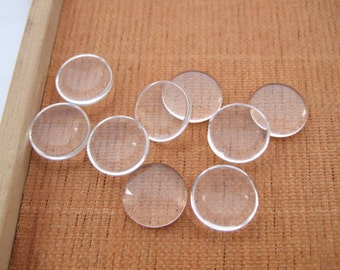 May include: Eight clear glass cabochons, round and smooth, arranged on a brown textured surface.
