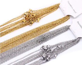 May include: Close-up of several gold and silver stainless steel chain necklaces with lobster claw clasps. The chains are displayed in a diagonal arrangement against a white background. The text "Stainless steel" is visible on a white tag.