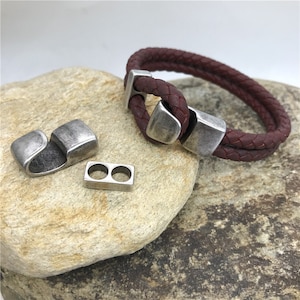 May include: A braided leather bracelet with a silver-toned clasp and two silver-toned spacers. The bracelet is maroon in colour.
