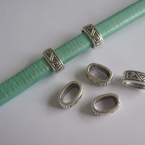 Peut inclure: Cinq perles ovales en métal argenté avec un motif géométrique. Les perles sont sur une surface vert clair.