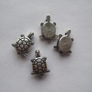 May include: Four silver turtle charms with detailed shell designs. The turtles are about 1 inch in size and have a loop at the top for attaching to jewelry or other crafts.